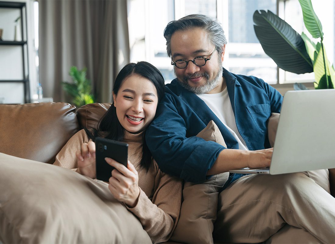 Read Our Reviews - Husband and Wife Looking at a Phone While Smiling on Their Living Room Couch